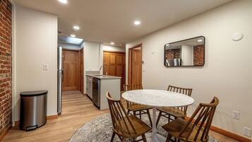 A modern kitchen with wooden cabinets, a stainless steel refrigerator, and a dining area with a round table and wooden chairs.