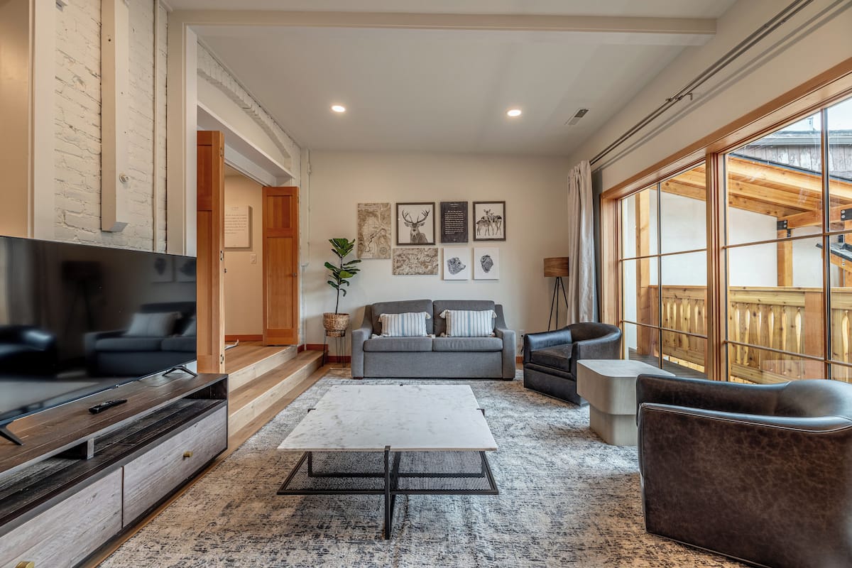 A spacious living room with a grey sofa, a coffee table, and a TV on a wooden stand.