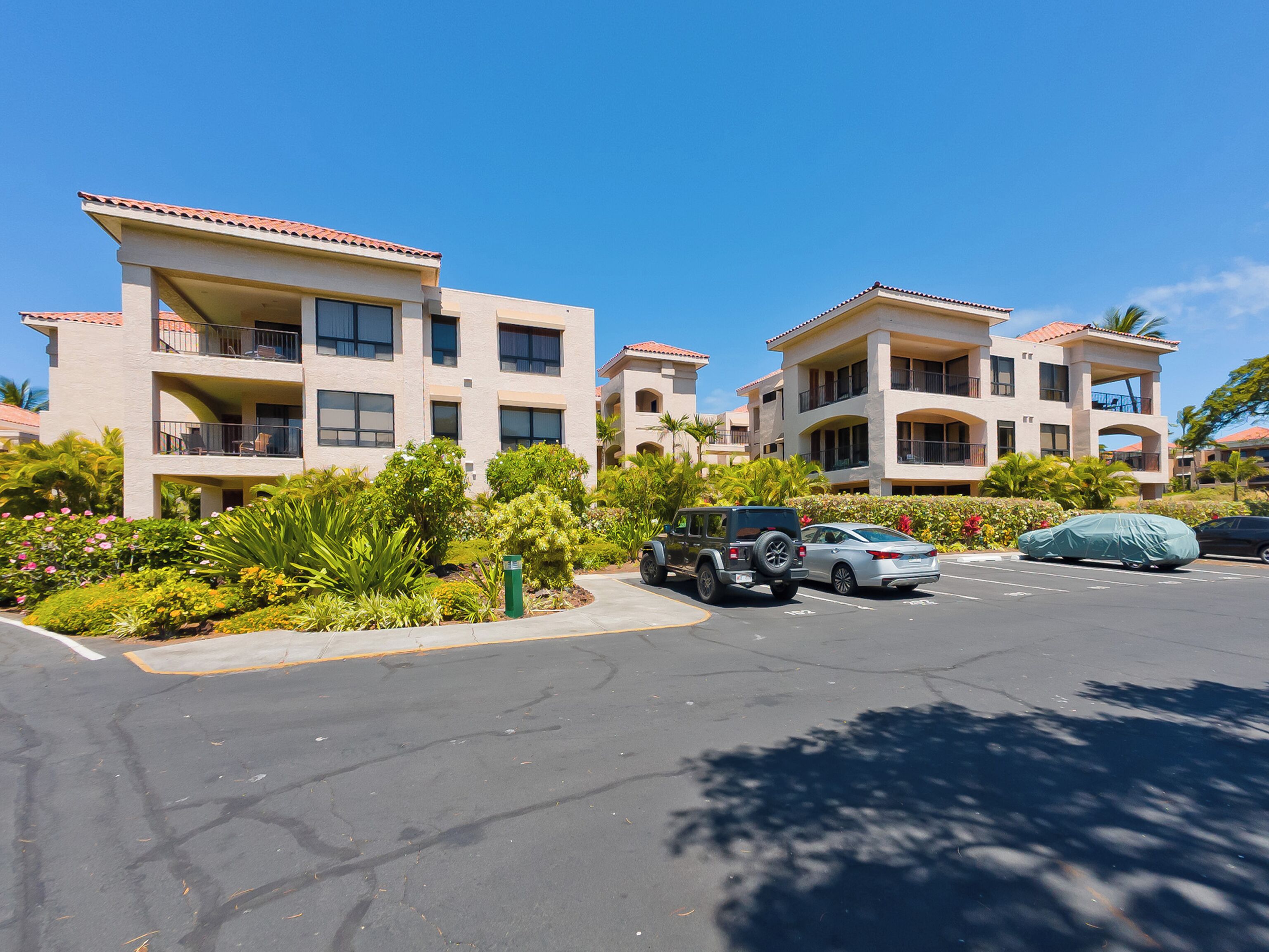 A multi-story hotel with balconies, a parking lot, and lush landscaping.