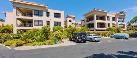 A multi-story hotel with balconies, a parking lot, and lush landscaping.