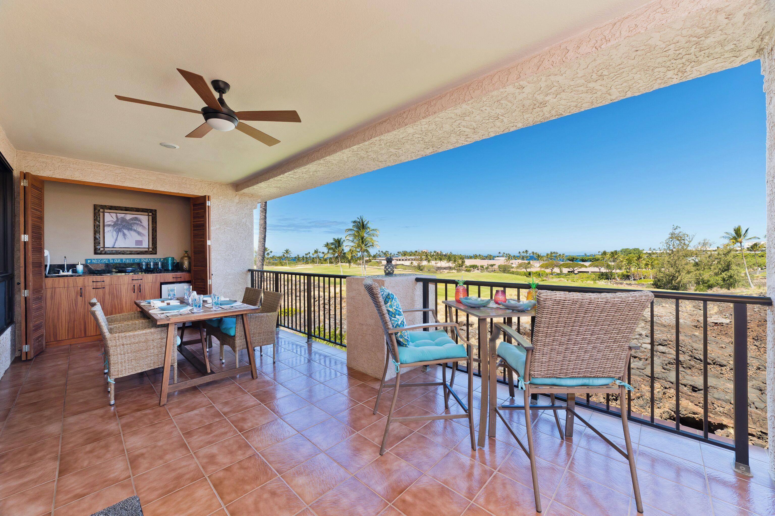 A balcony with a dining area, a ceiling fan, and a view of a landscape with trees and a clear sky.