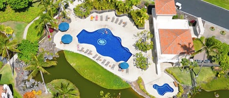 Vista aérea de un resort con una piscina grande, áreas de descanso y un estanque pequeño.