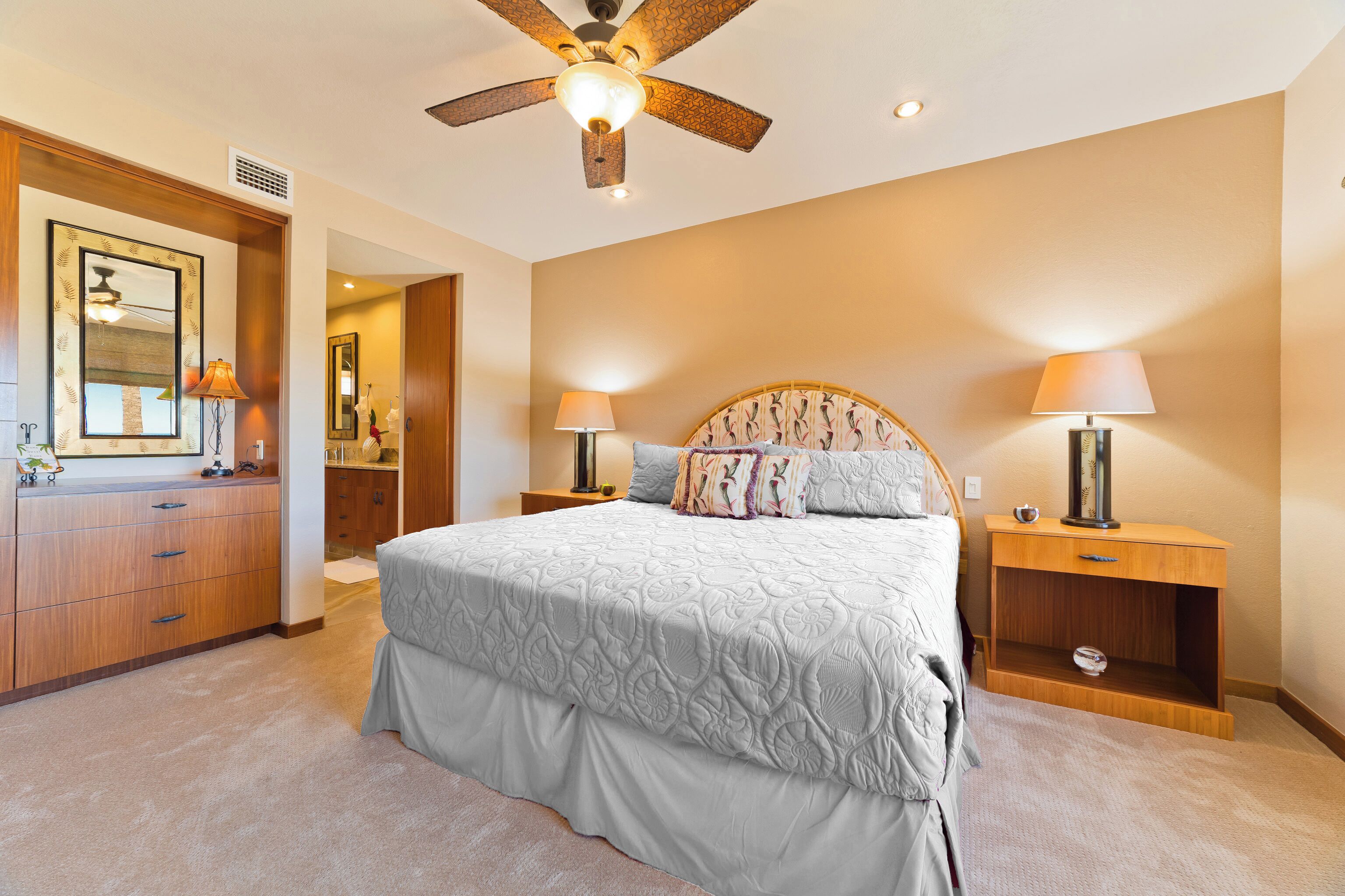 A bedroom with a large bed, wooden nightstands, a ceiling fan, and a mirror.
