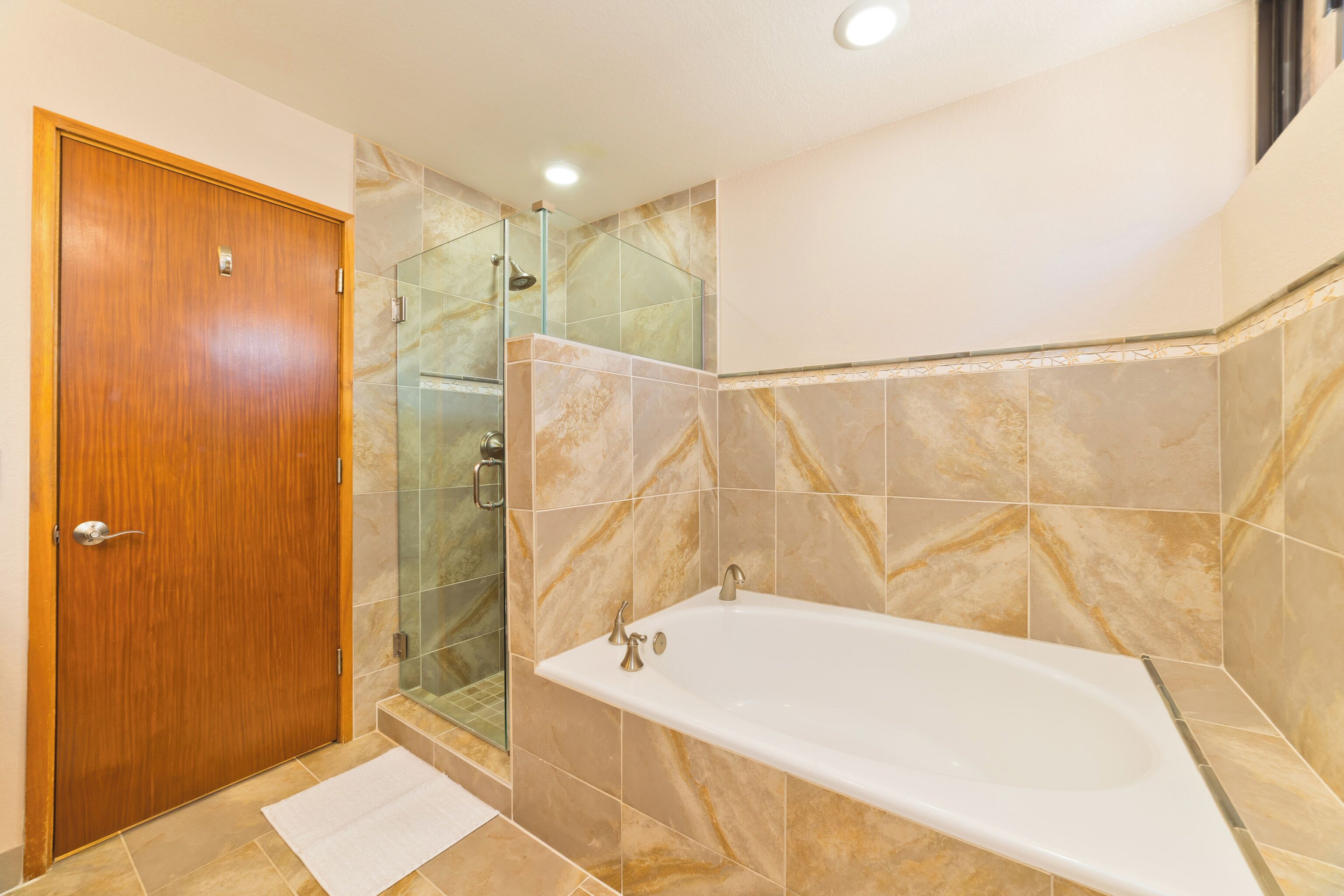 A bathroom with a wooden door, a glass shower enclosure, and a white bathtub.