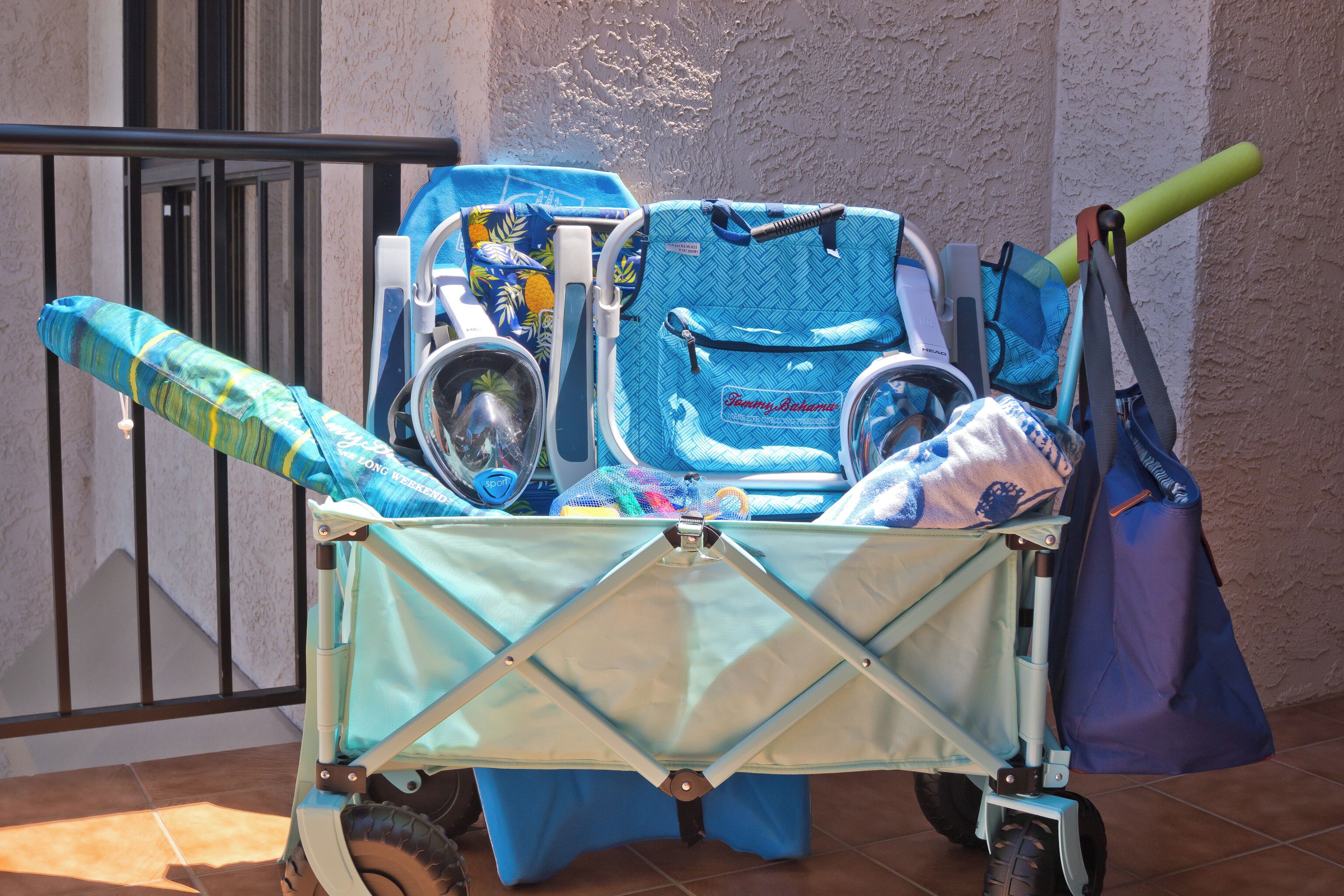 A luggage cart filled with various items including a blue suitcase, a stroller, and a blue bag.
