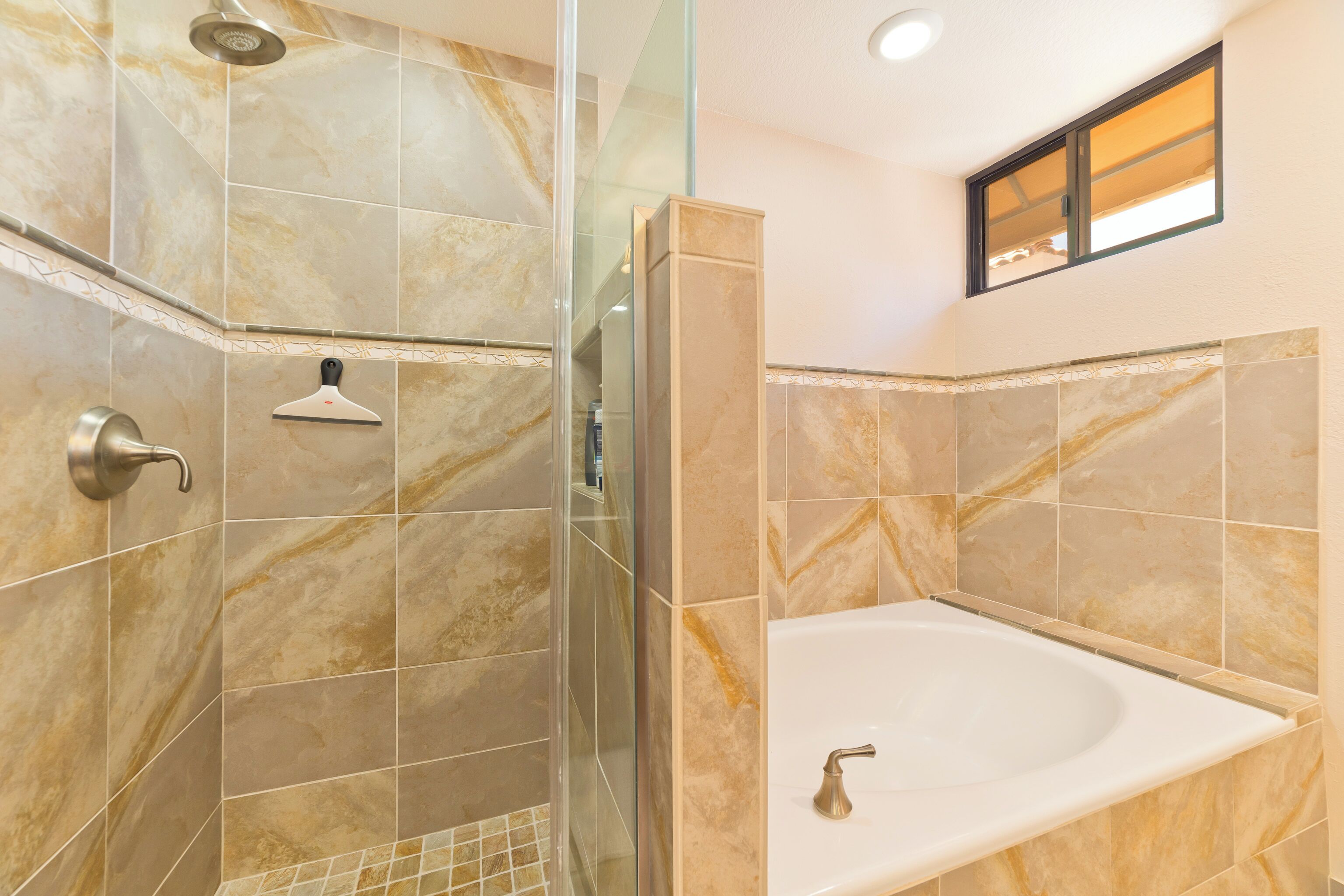 Un baño con ducha acristalada, bañera y azulejos de mármol.