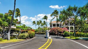 A hotel entrance with a paved driveway, palm trees, and a building with a tiled roof.