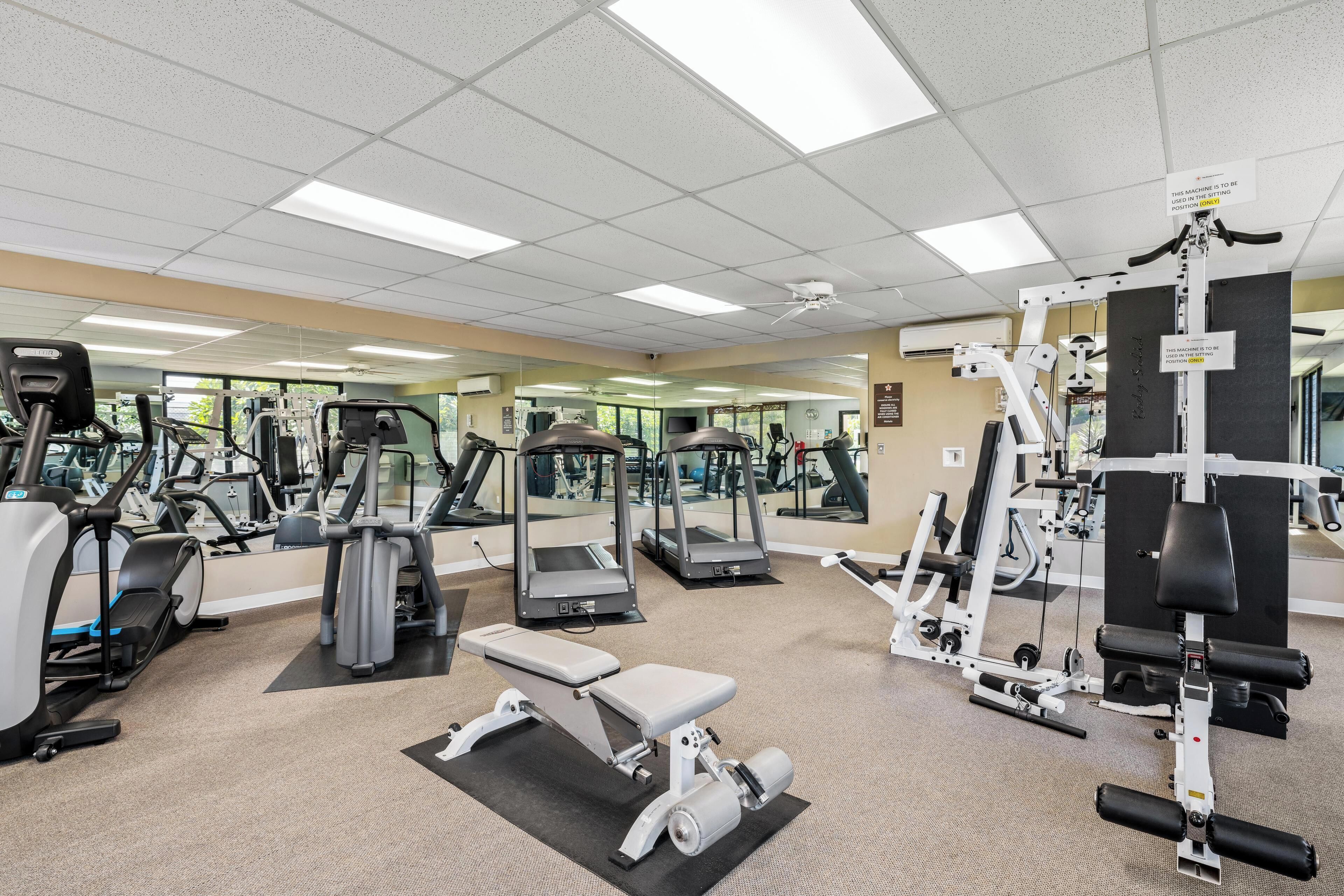 Et fitnessrum med forskellig træningsudstyr, herunder løbebånd, styrkemaskiner og en bænk.