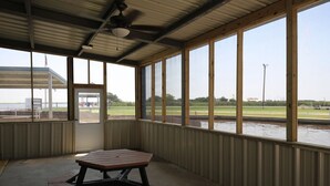 Un espace pique-nique abrité, équipé d’une table et de bancs, de grandes fenêtres et offrant une vue sur un terrain de sport.