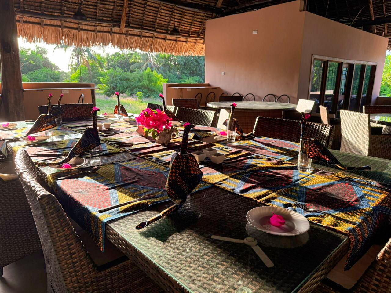 A dining area with a table set for four, featuring a colorful tablecloth and wicker chairs.
