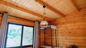Quarto de cabana de madeira com uma janela grande, luminária pendente e um ventilador.