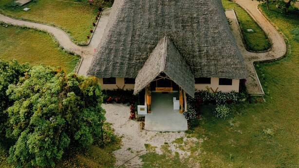 A thatched-roof building surrounded by lush greenery and palm trees, with a view of the sea in the background. - Signature Collection by Eight Continents, Mafia Island (Mafia Island)