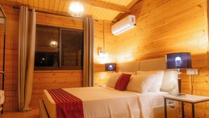 A wooden cabin room with a bed, bedside lamps, and an air conditioning unit. - Signature Collection by Eight Continents, Mafia Island (Mafia Island)