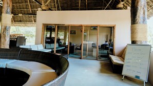 A reception area with a whiteboard displaying meal times, wicker furniture, and a thatched roof structure. - Signature Collection by Eight Continents, Mafia Island (Mafia Island)