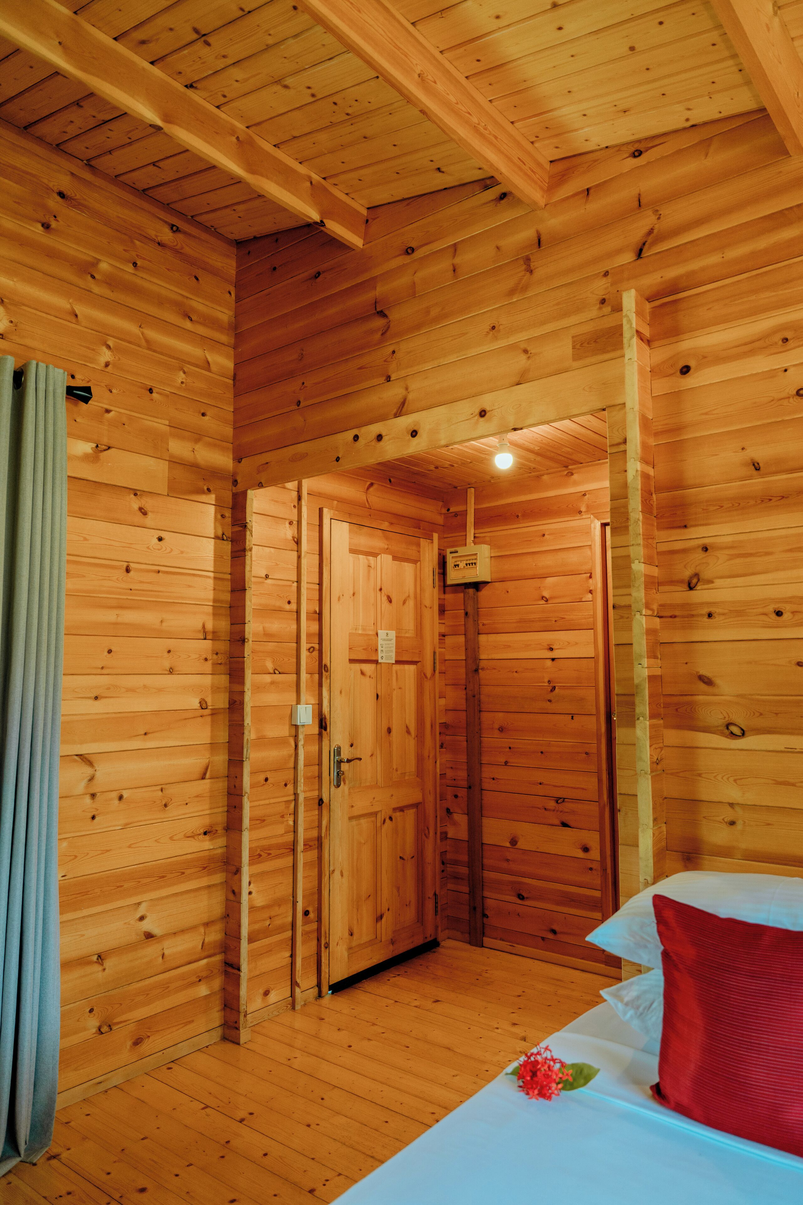 A wooden cabin room with a bed, a door, and a small window.