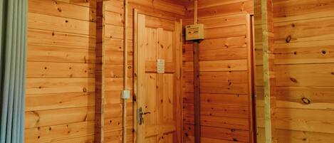 A wooden cabin room with a bed, a door, and a small window.