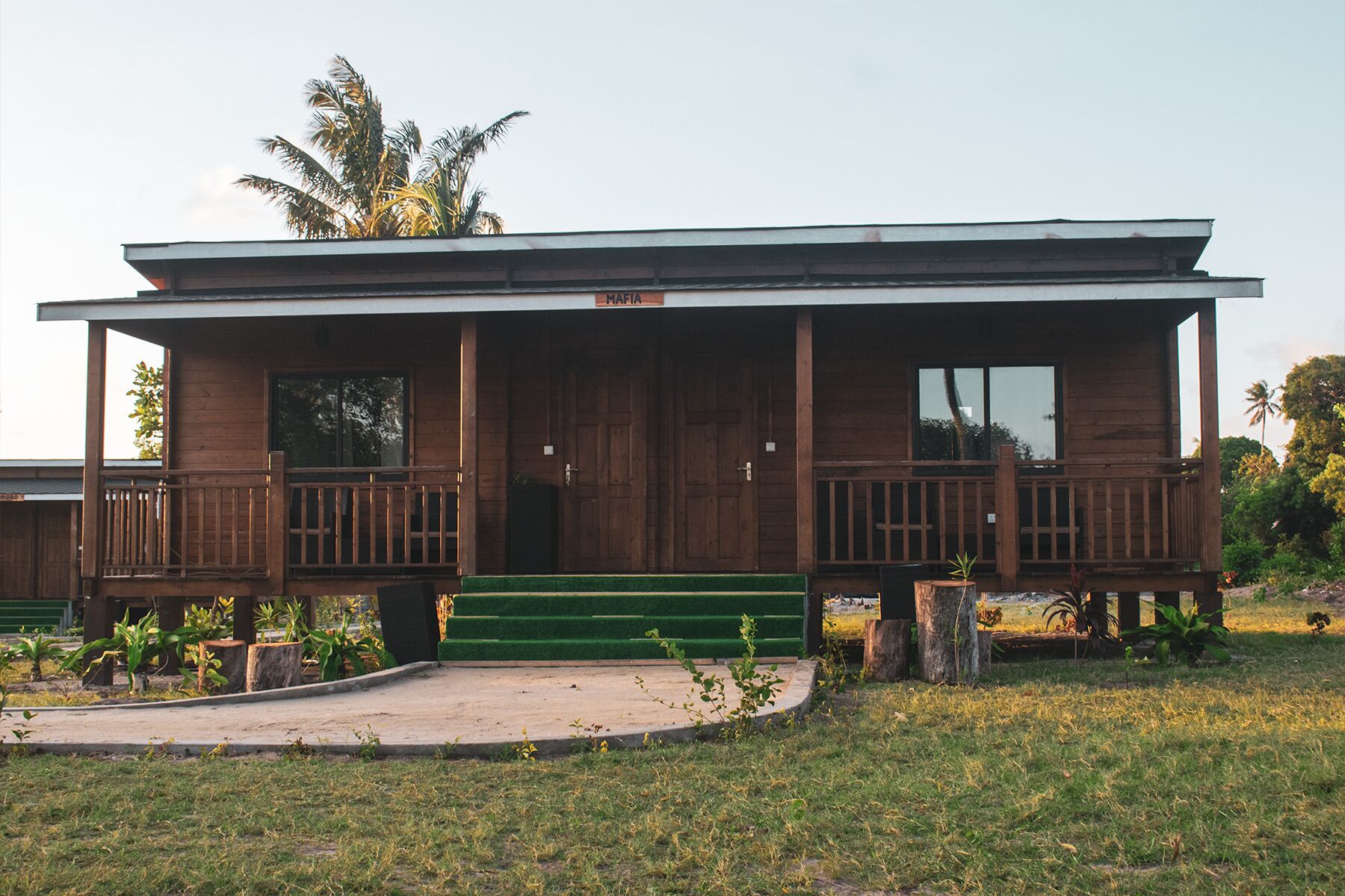 A wooden building with a balcony, a green lawn, and a palm tree in the background.