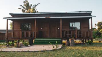 A wooden building with a balcony, a green lawn, and a palm tree in the background.