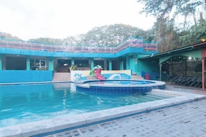 Una piscina con idromassaggio, una zona relax coperta e un edificio con facciata blu.