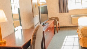 Une chambre d’hôtel avec un lit, un bureau avec une lampe, une télévision et une chaise.