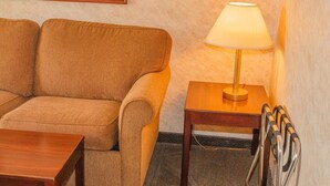 Une pièce chaleureuse avec un canapé beige, une table d’appoint en bois sur laquelle se trouve une lampe, et un tableau encadré accroché au mur.