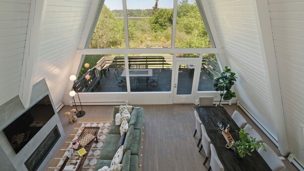A cozy interior with a fireplace, a sofa, a dining table, and a view of the deck and greenery outside. - The Gnome Gully - A-Frame w/ Sound Views (Olympia)