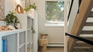 A narrow hallway with white shelving units, a wooden staircase, and a window with a view of trees. - The Gnome Gully - A-Frame w/ Sound Views (Olympia)