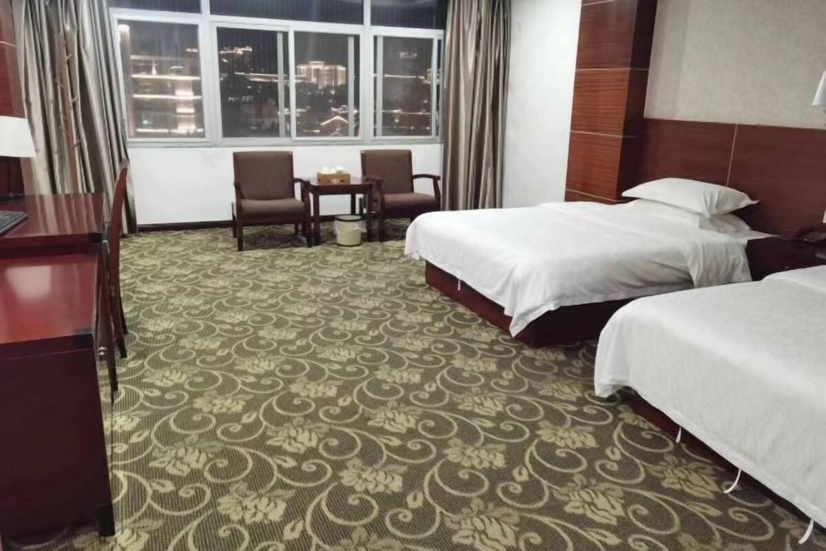 A hotel room with two beds, a desk, a chair, a small table, and a window with curtains.