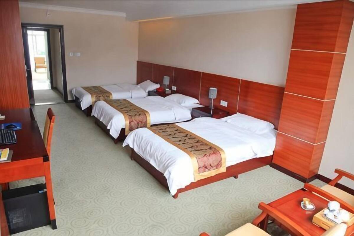A hotel room with three beds, a wooden desk, a small table, and a chair.