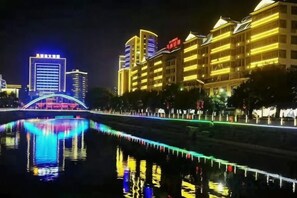 A nighttime cityscape with illuminated buildings, a reflective water body, and a bridge. - Tianxin Business Hotel (Wuping)