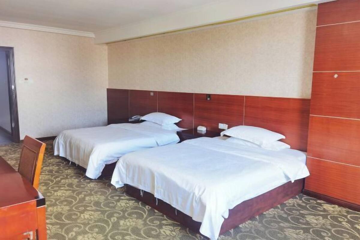 A hotel room with two beds, a wooden headboard, a desk, and a patterned carpet.