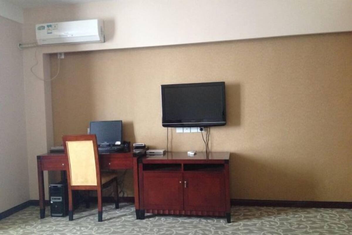A hotel room with a desk, chair, television, and a cabinet.