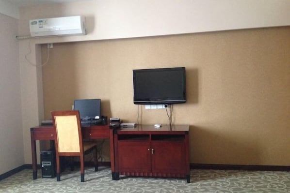 A hotel room with a desk, chair, television, and a cabinet.
