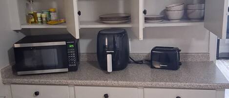 Une cuisine compacte équipée d’un four à micro-ondes, d’une machine à café, d’un grille-pain et d’étagères contenant de la vaisselle et des ustensiles de cuisine.