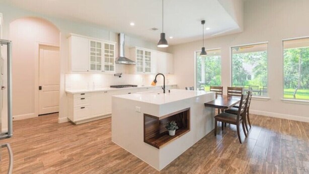 A modern kitchen with a central island, white cabinetry, and a dining area with a table and chairs. - New 4bdr in Gated Comm + HUGE Summer Kitchen Area (Tomball)
