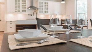 A modern kitchen with white cabinets, a dark countertop, and a dining area with a wooden table set for four. - New 4bdr in Gated Comm + HUGE Summer Kitchen Area (Tomball)