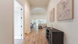 A spacious hallway with wooden flooring, a dark wooden console table, and abstract paintings on the wall. - New 4bdr in Gated Comm + HUGE Summer Kitchen Area (Tomball)