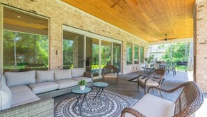 A covered outdoor patio with a brick wall, large windows, wicker furniture, and a ceiling fan. - New 4bdr in Gated Comm + HUGE Summer Kitchen Area (Tomball)