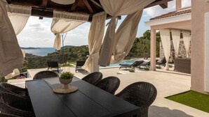 Eine Terrassensitzgruppe im Freien mit Tisch und Stühlen, mit Blick auf einen Pool und eine schöne Meerlandschaft.