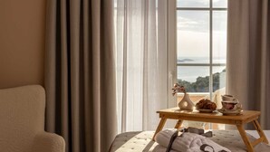 Ein Schlafzimmer mit Bett, Nachttisch mit Vase und Tasse, und Meerblick durch ein Fenster.