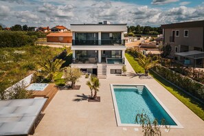 A modern two-story house with a swimming pool, surrounded by greenery and other residential buildings. - Luxurious 3-BR spa villa with heatable pool close to beaches (Poreč)