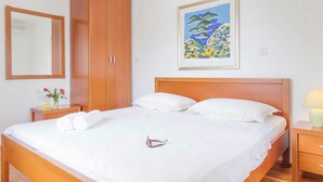 A bedroom with a wooden bed, white linens, a wooden wardrobe, a bedside table with a lamp, and a framed painting on the wall. - Charming 3-BR Villa for 6 with private pool, close to the sea (Sumartin)