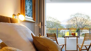 Hotellihuone, jossa on sänky, tyynyjä, juomien kanssa tarjoiltava pöytä ja parveke, jolta on näkymä.