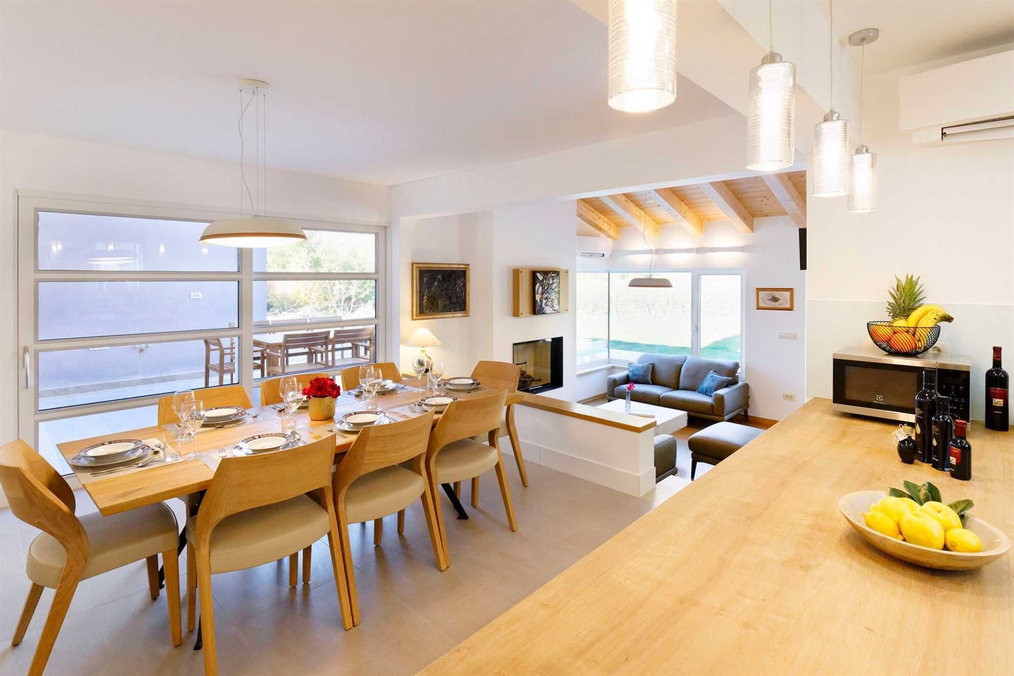 A modern kitchen with a wooden dining table set for six, a sofa, and a fruit bowl on the counter.