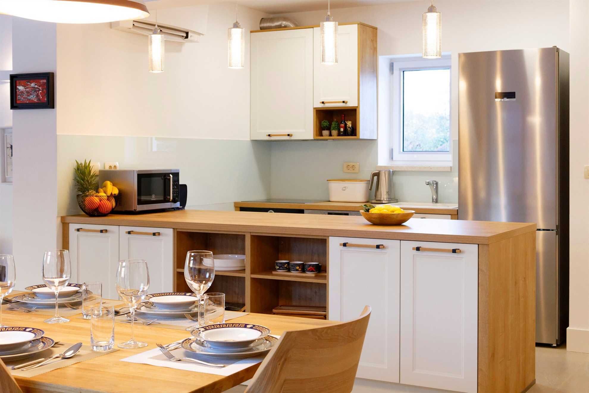 A modern kitchen with white cabinets, a stainless steel refrigerator, and a wooden dining table set for four.