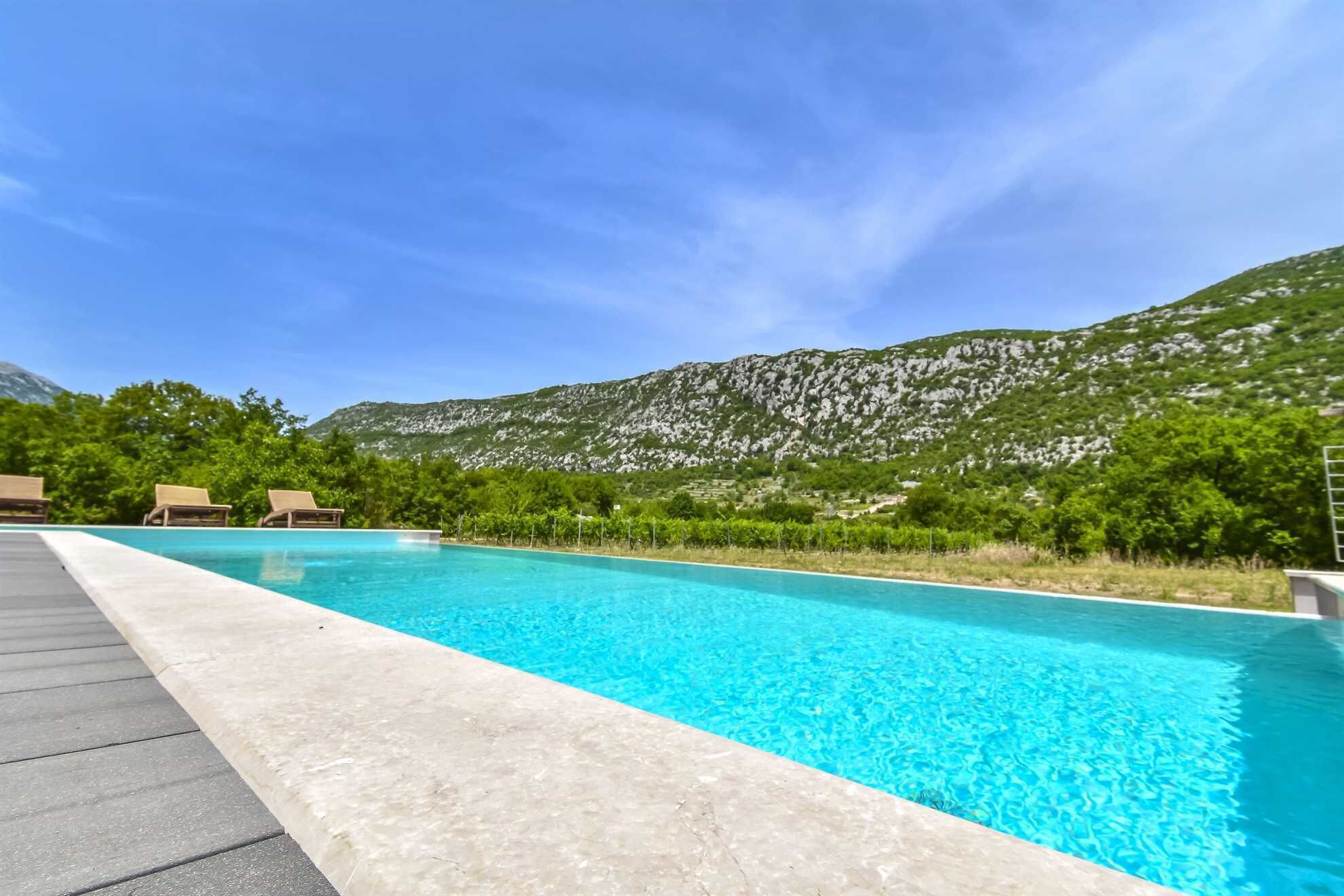 A swimming pool with lounge chairs and a mountainous backdrop.