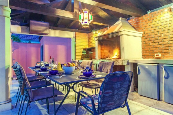 An outdoor dining area with a brick wall, a grill, and a table set for a meal.