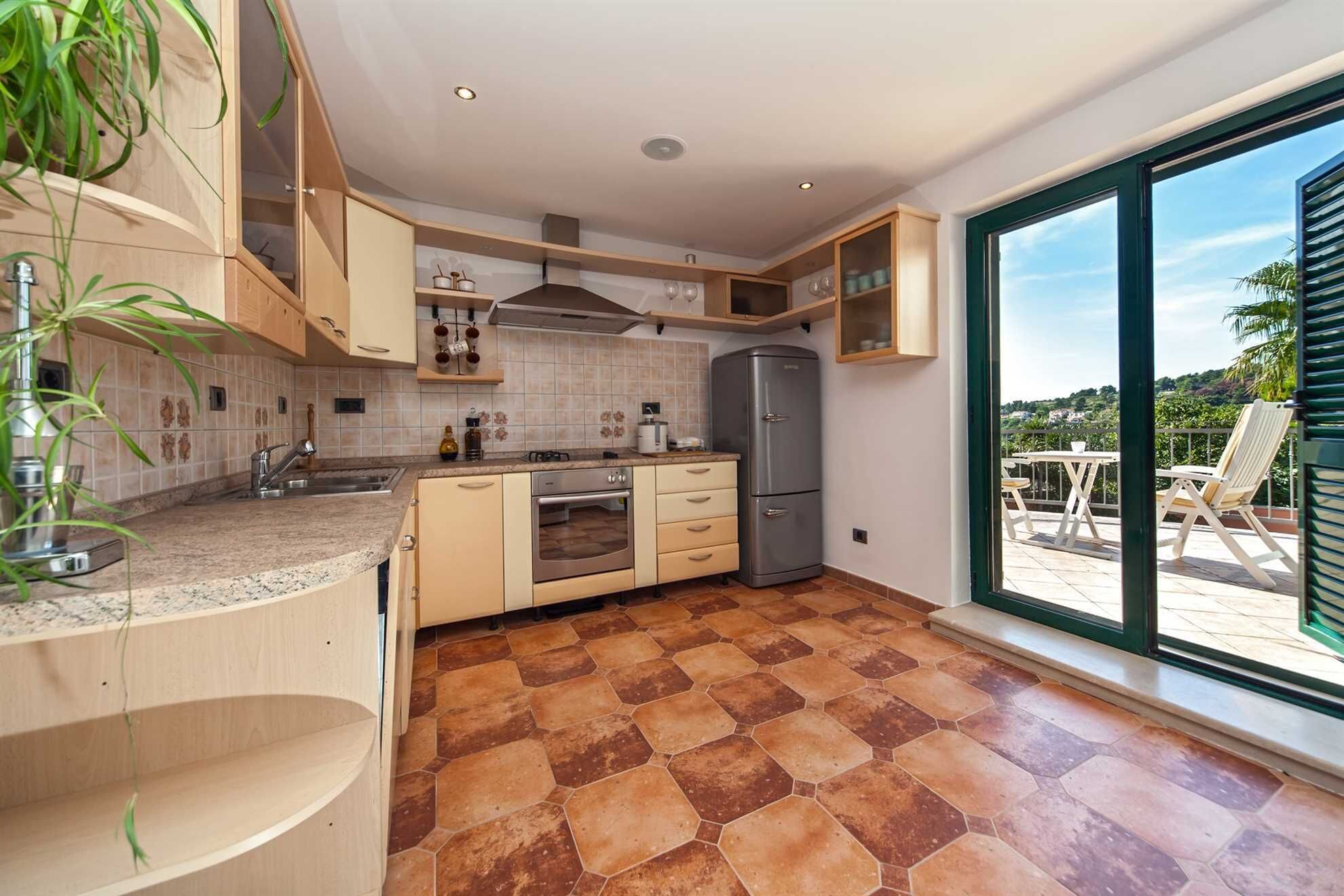 A modern kitchen with a large window, a built-in oven, and a refrigerator.
