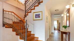 A staircase with wooden steps and metal balusters, a framed picture on the wall, and a hallway with a mirror and a plant on a console table. - Spacious 4-BR Villa for 8+2 near the beach, with private pool (Sumartin)