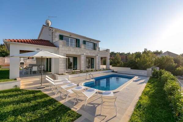 Ein zweistöckiges Haus mit Swimmingpool, Gartenmöbeln und einer Satellitenschüssel.